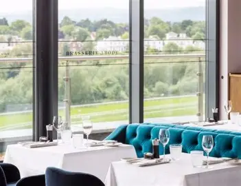 Restaurant dining area with teal banquette seating, white-clothed tables and views over greenery.