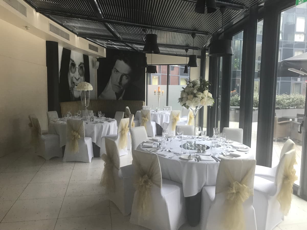 Private dining room at Abode Chester laid for a wedding breakfast with white chair covers and tall floral centrepieces.