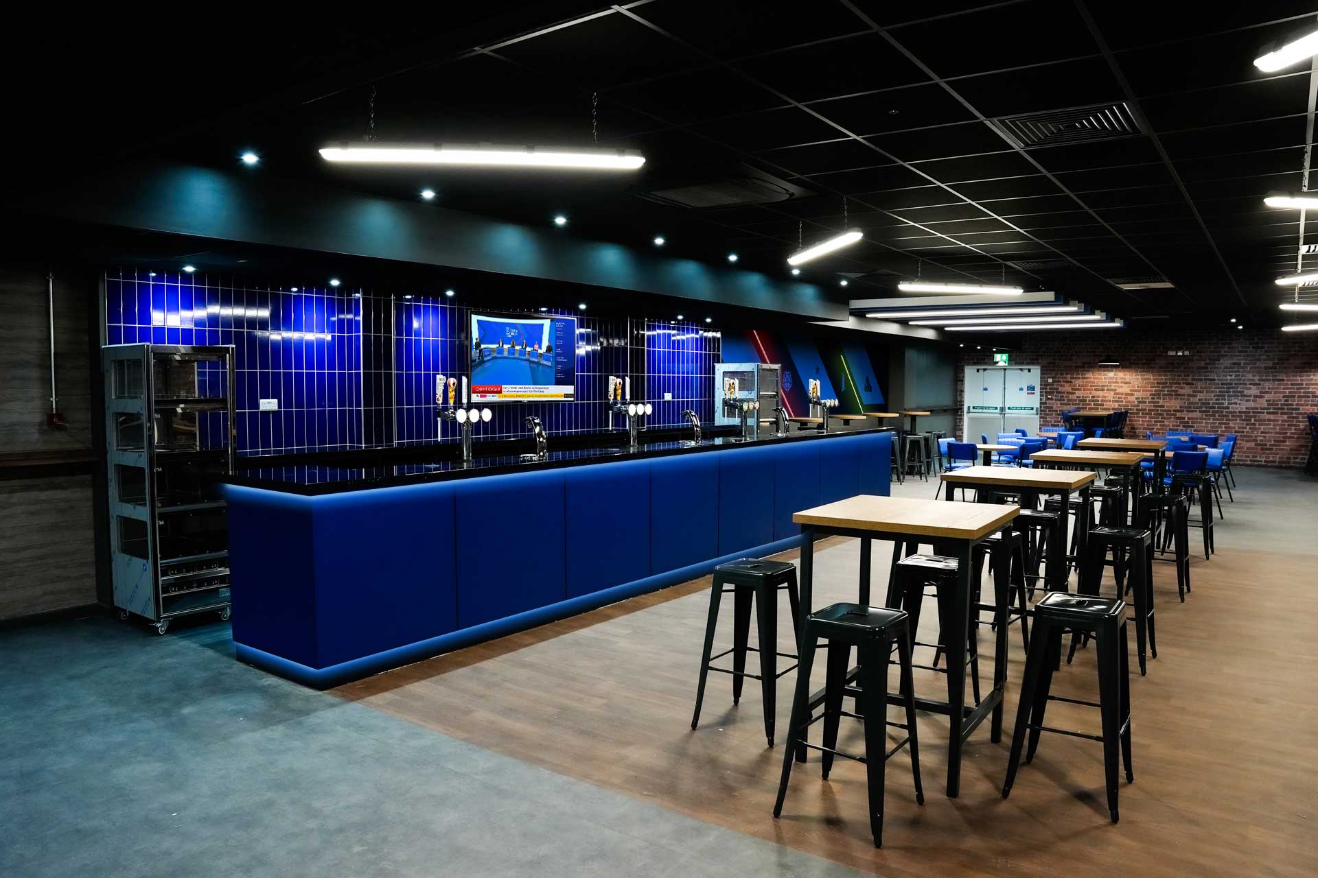 Bar area with blue tiled frontage, draft taps and high wooden tables with stools.