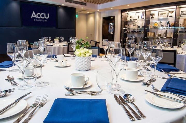 Formally laid round dining tables with blue napkins and white flowers at Accu Stadium.