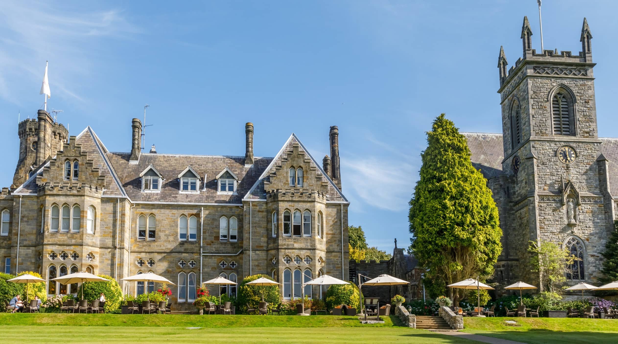 Exterior of a Gothic stone country house hotel with manicured lawns and a church tower