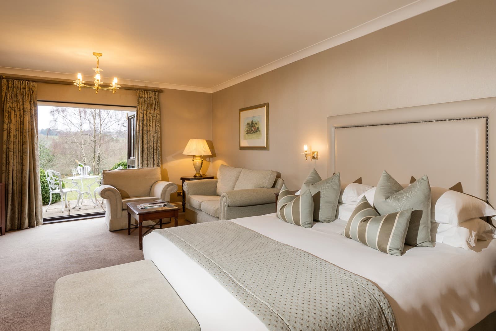 Spacious hotel bedroom with double bed, seating area and countryside views beyond patio doors.