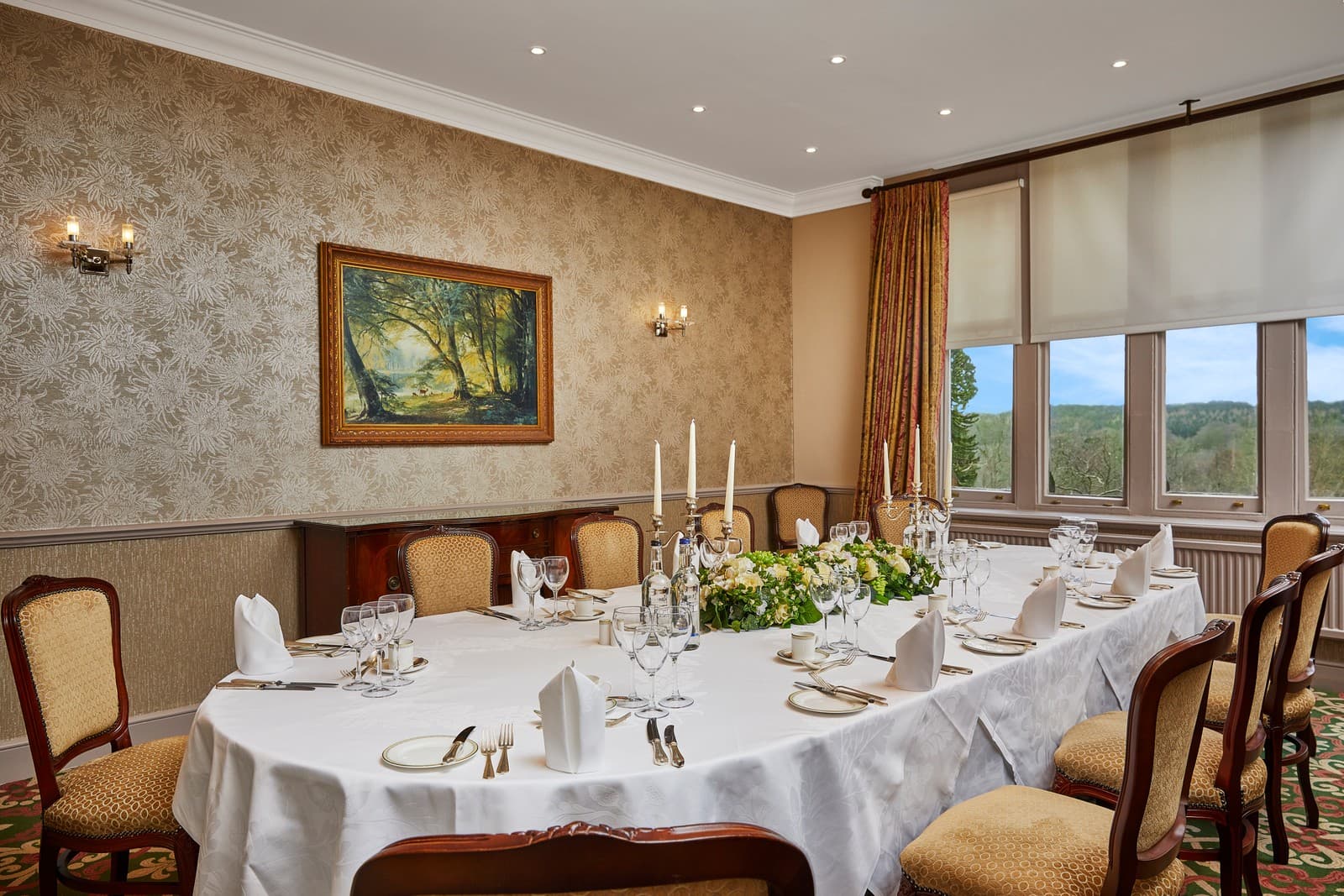 Private dining room with oval table laid for a formal meal and woodland views.