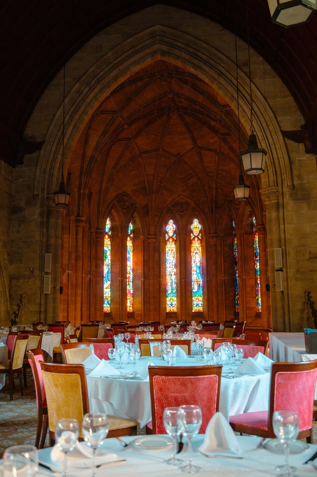 Dining room with Gothic stone arches, stained glass windows and white-clothed tables set with glassware.