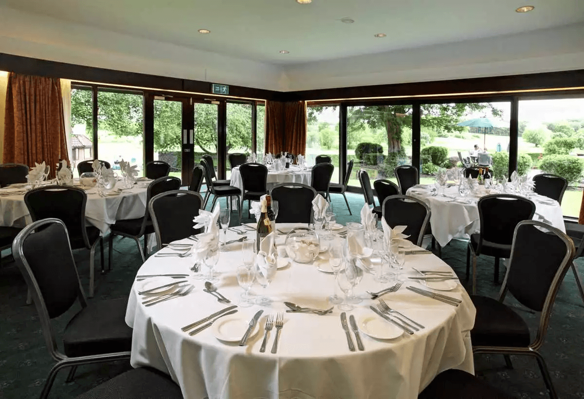 Banqueting room at Barnham Broom Hotel with round tables set for a formal meal and garden views.