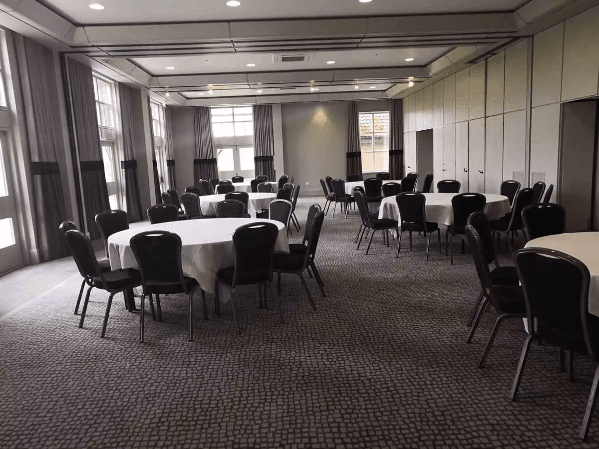 Banqueting suite at Barnham Broom Hotel laid with round white-clothed tables and black chairs.