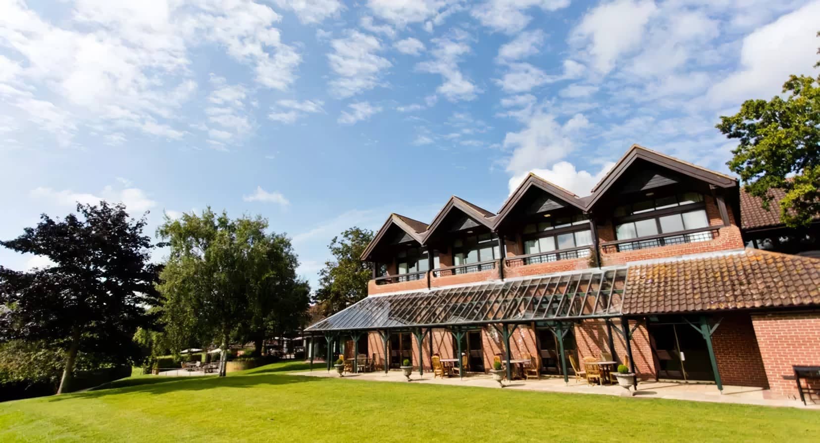 Exterior of Barnham Broom Hotel showing red brick building, glass canopy terrace and lawned gardens.