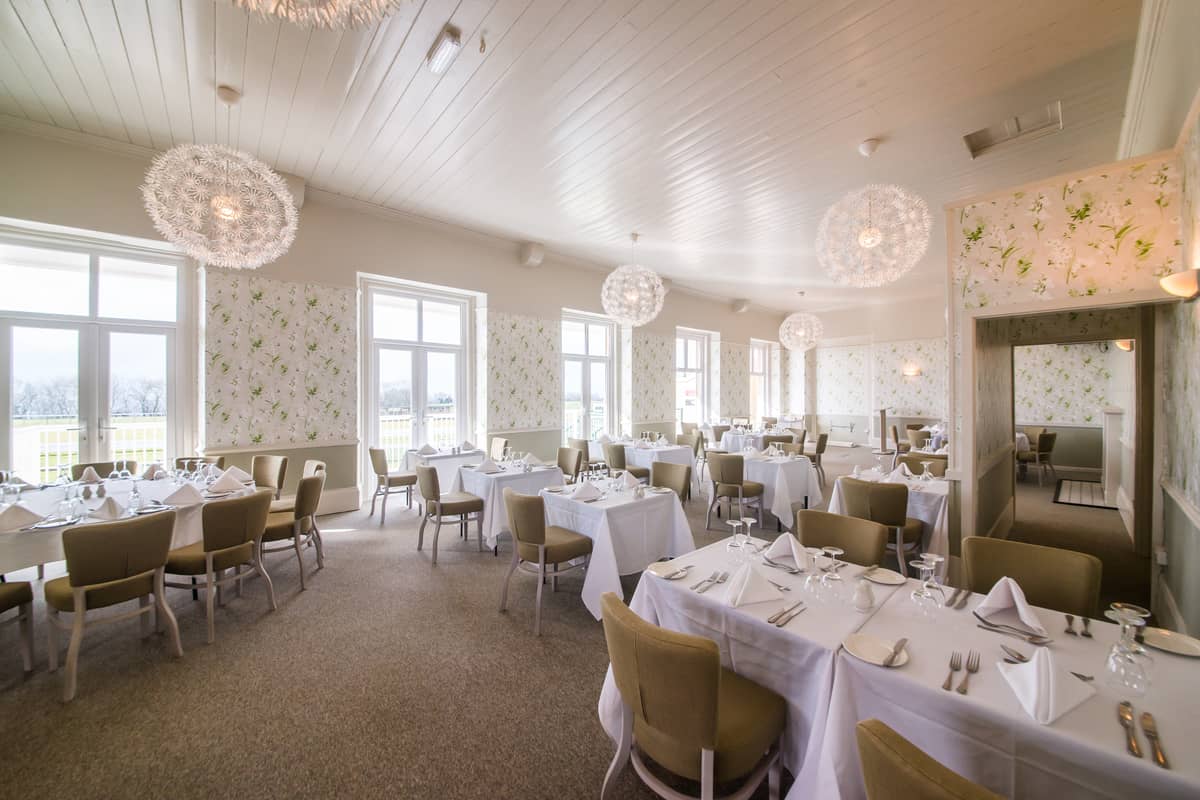 Bright dining room with white tablecloths, olive chairs and dandelion-style pendant lights.
