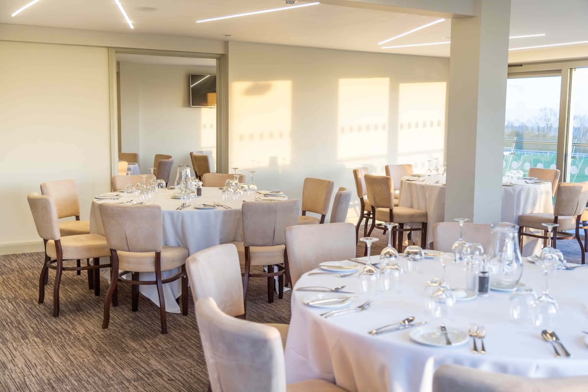 Bright private dining room with round tables laid with white linen and glassware at Bath Racecourse.