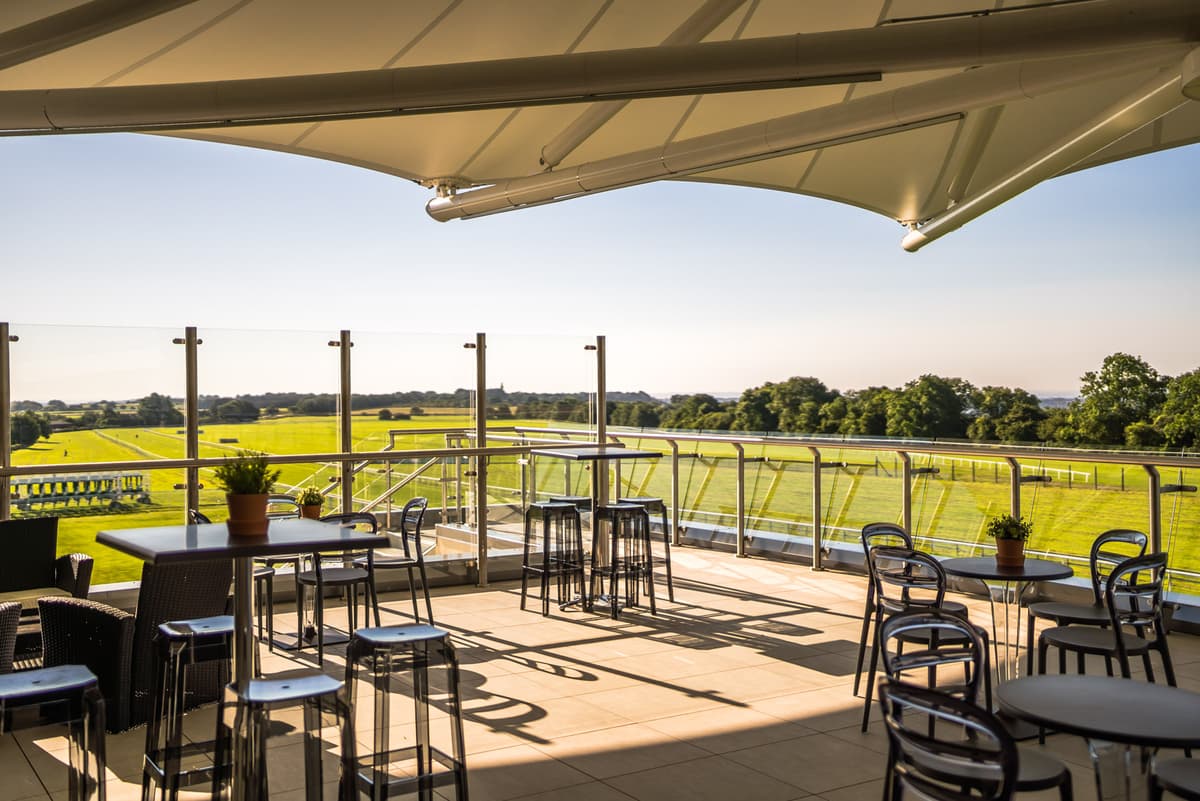 Elevated terrace with bar-height tables overlooking the racecourse and open countryside beyond.