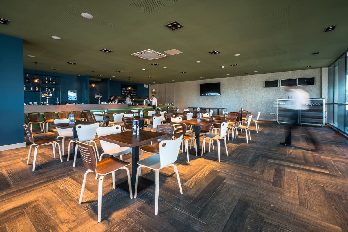Spacious bar and dining area with wooden tables, white chairs and herringbone flooring.