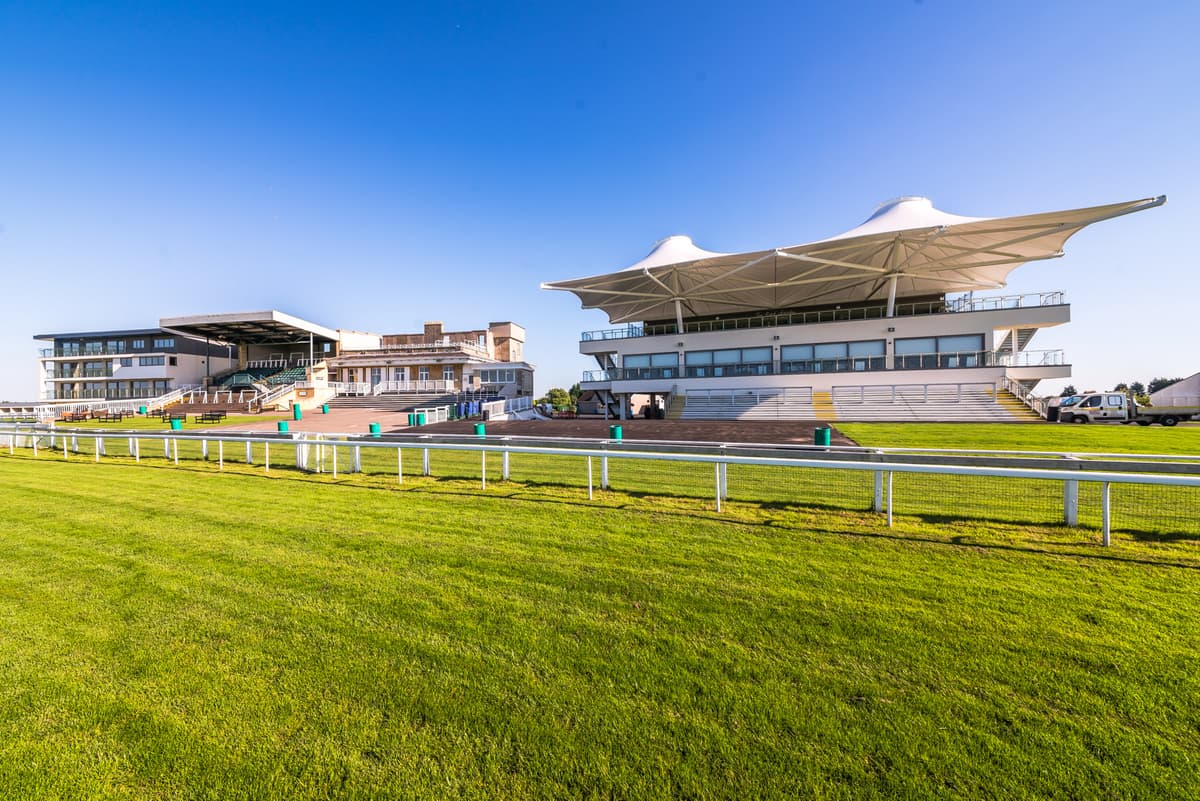 Exterior view of Bath Racecourse grandstands and white tensile canopy roof on a sunny day.