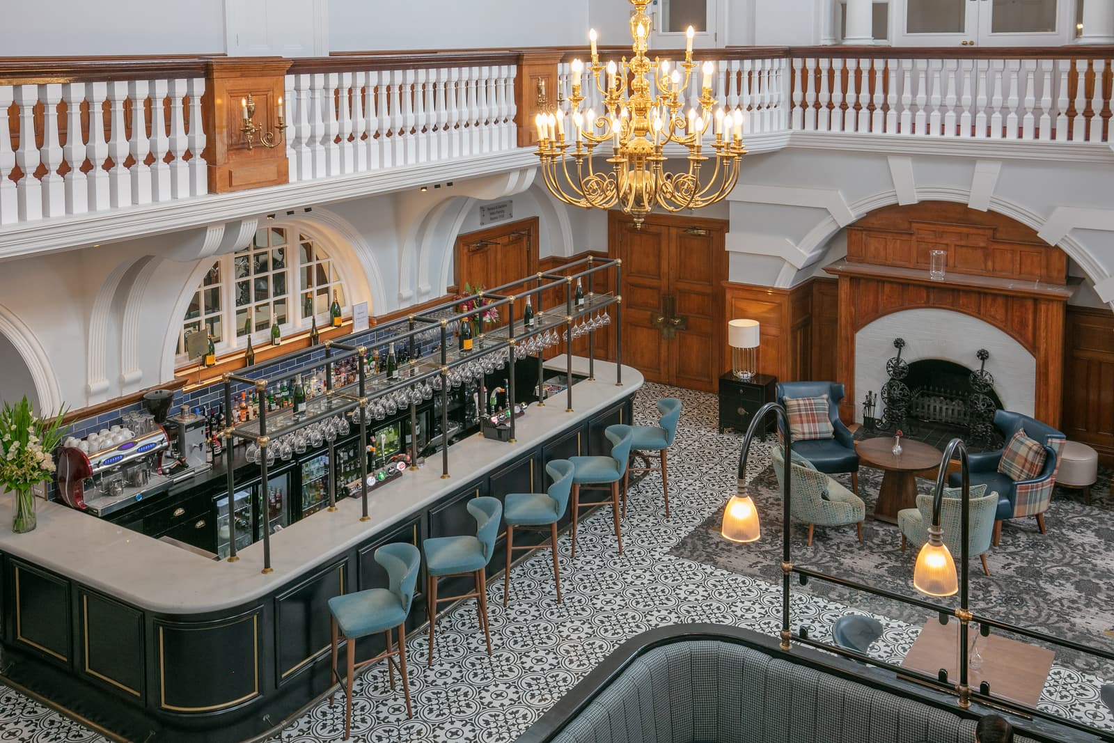 Grand hotel bar with blue stools, patterned tiled floor and gold chandelier above.