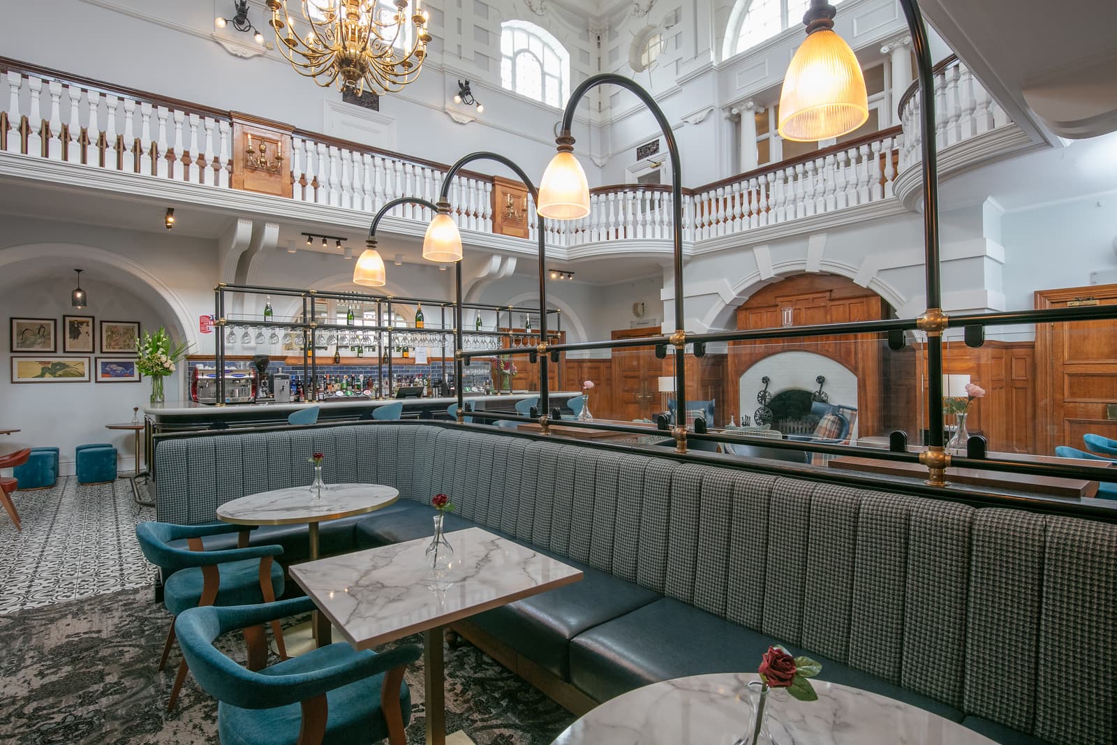 Grand bar interior with marble tables, houndstooth banquettes and a wraparound mezzanine gallery.