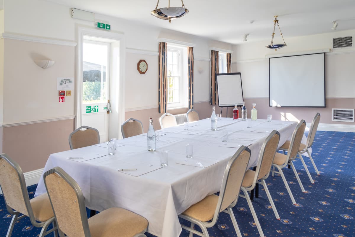 Conference room with long white-clothed table, chairs, flipchart and projection screen.