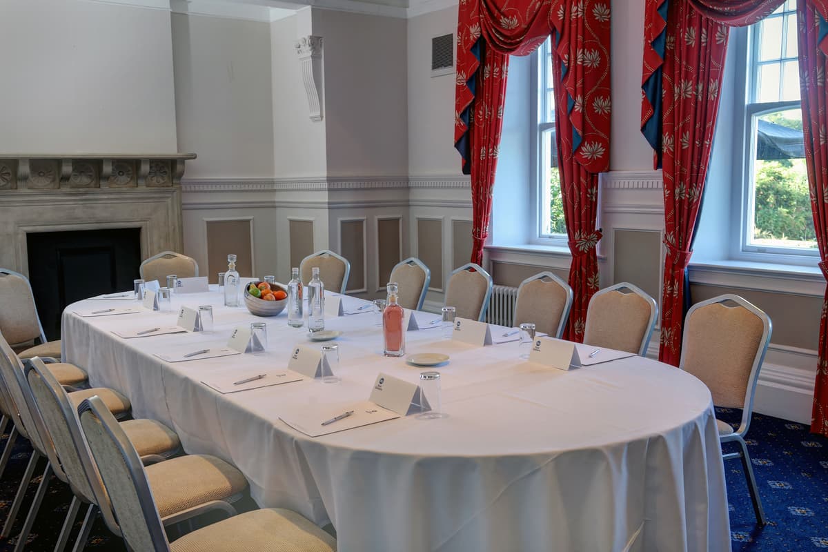 Boardroom style meeting room with white-clothed oval table, period fireplace and red curtains.