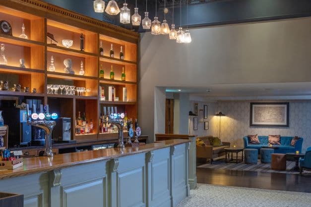 The hotel bar with brass taps, backlit shelving and a lounge seating area beyond.