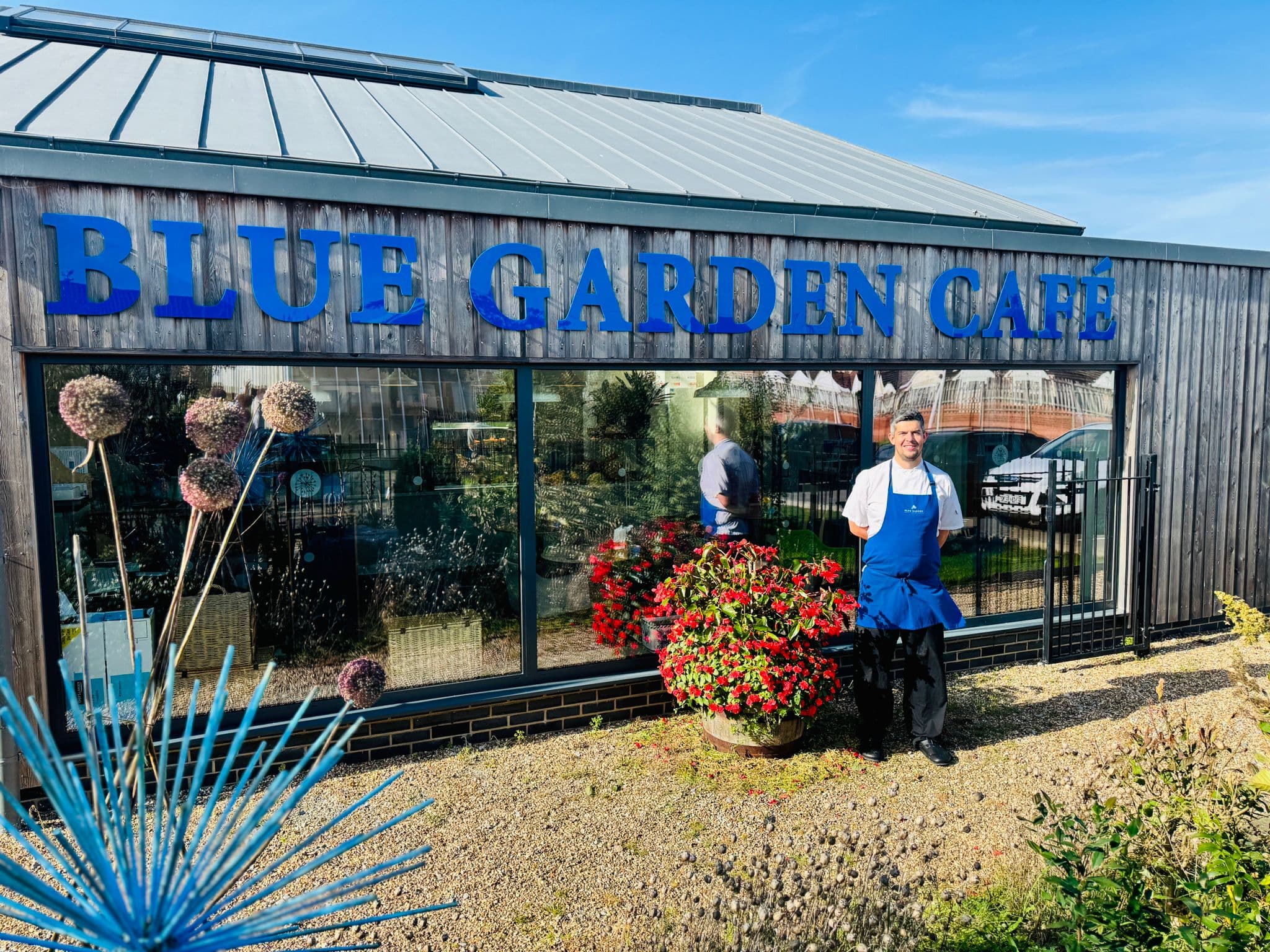 Chef in white jacket and blue apron standing outside Blue Garden Café, Clacton-on-Sea.