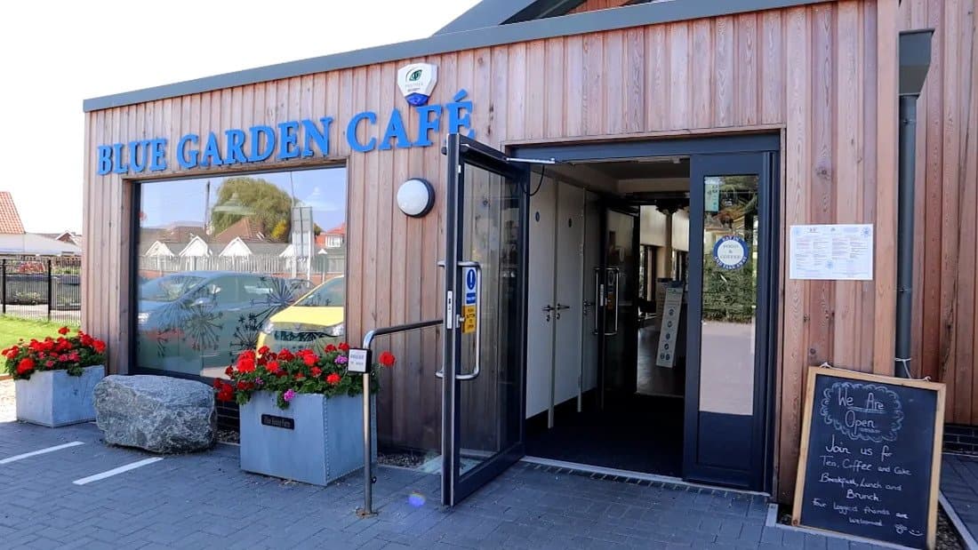Exterior of Blue Garden Café with timber cladding, open door and red flowers outside.