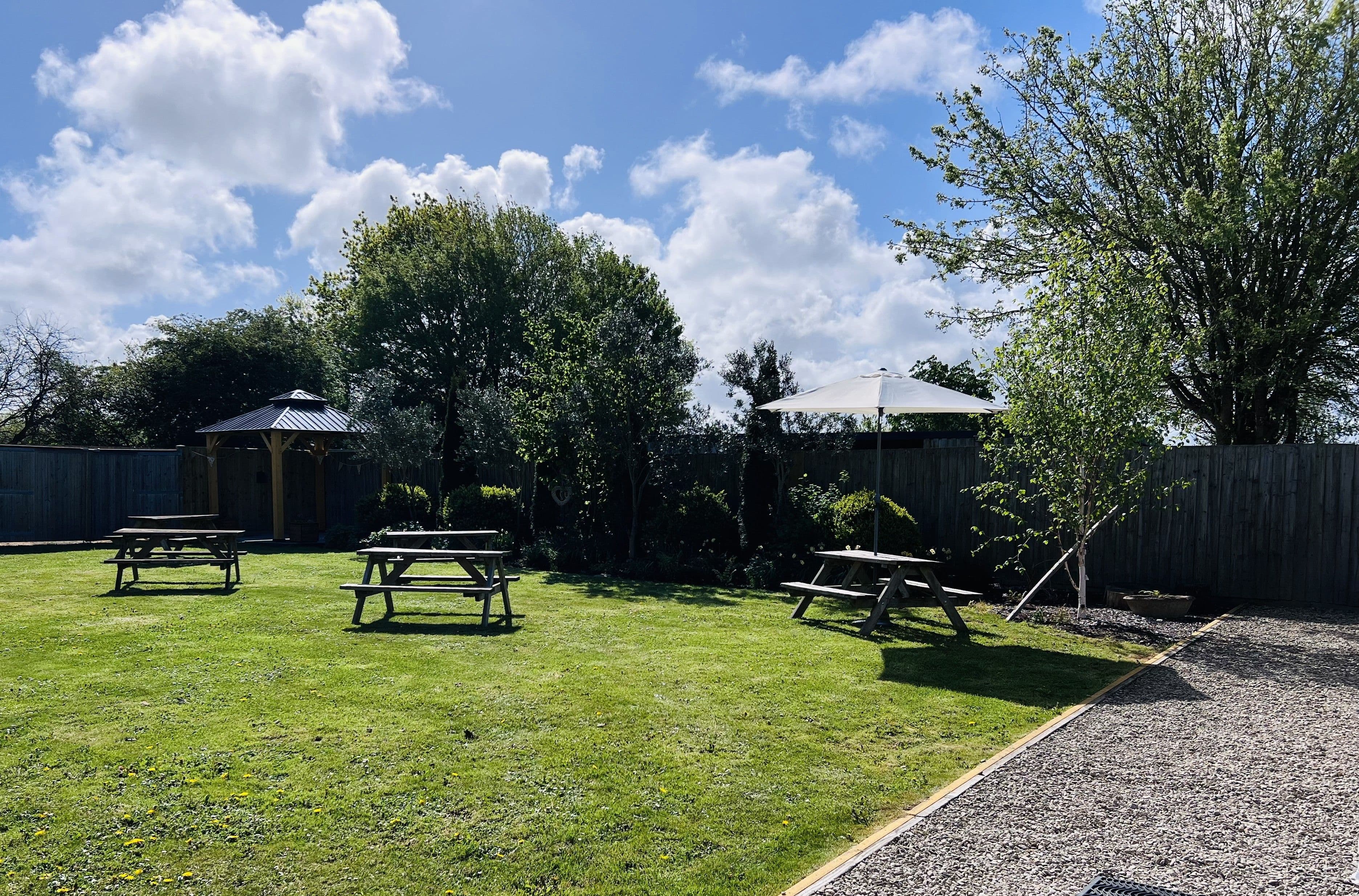 Lawned beer garden with wooden picnic benches, a gazebo and a parasol.