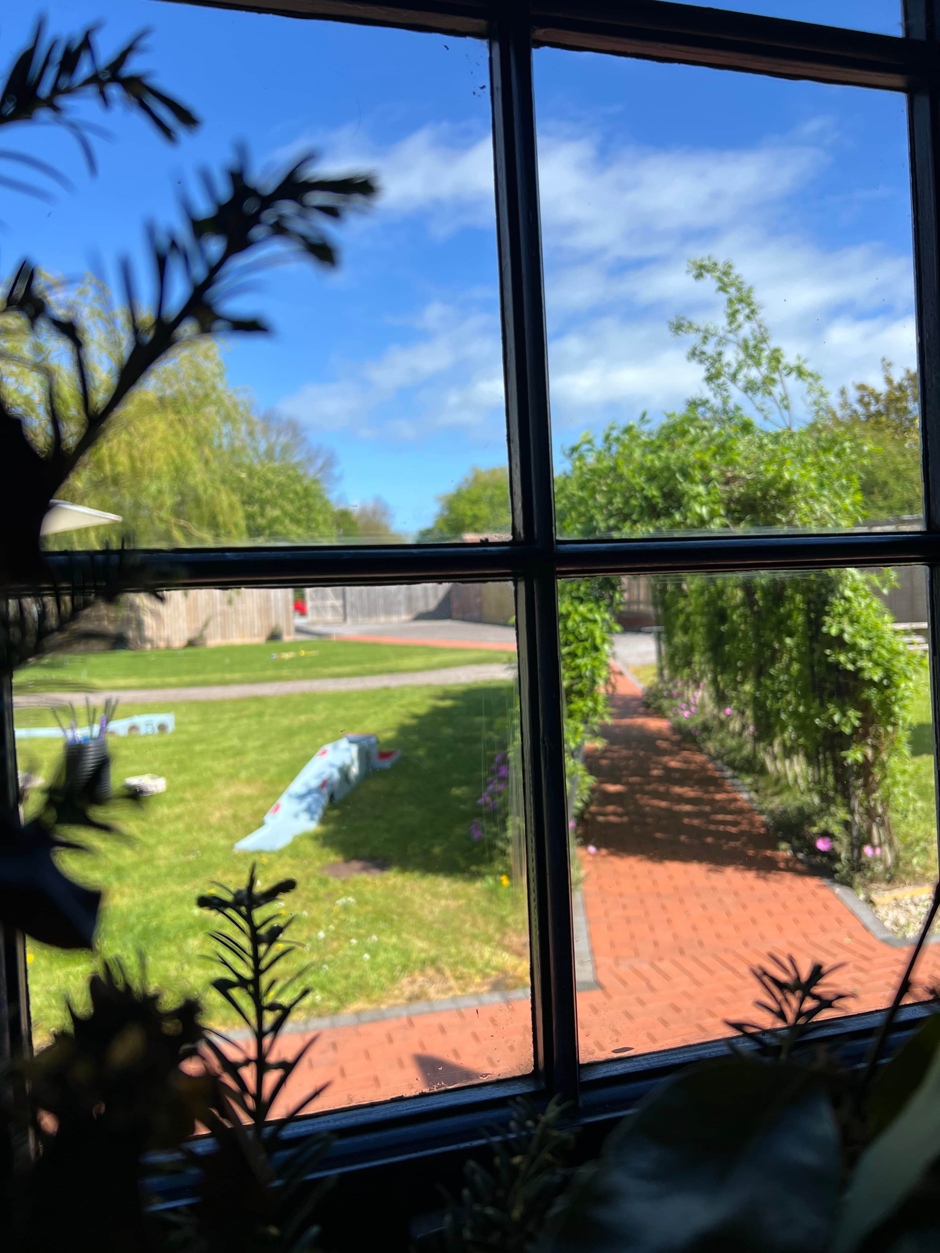 View through a sash window overlooking a garden with a red brick path and lawn.