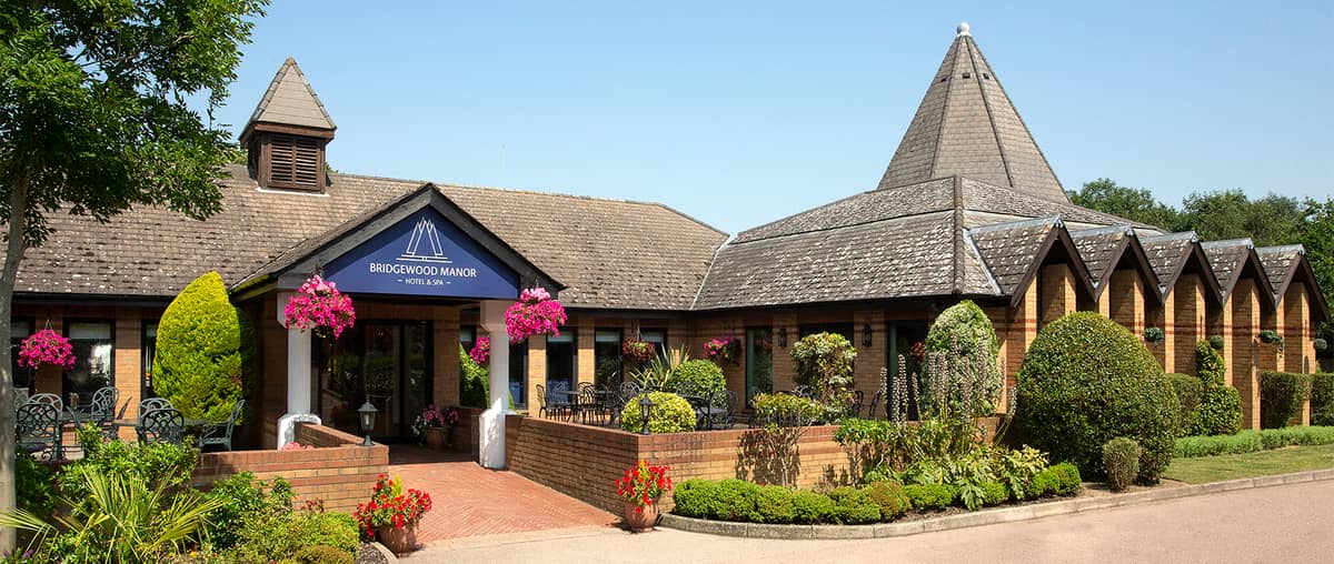 Exterior of Bridgewood Manor Hotel and Spa with hanging baskets and landscaped gardens.