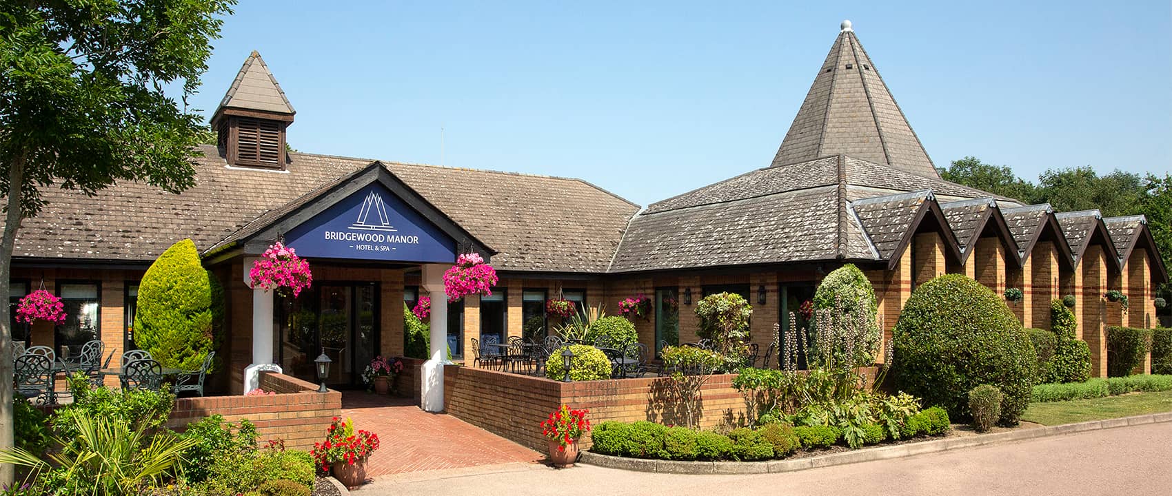 Exterior of Bridgewood Manor Hotel and Spa with hanging baskets and landscaped gardens.