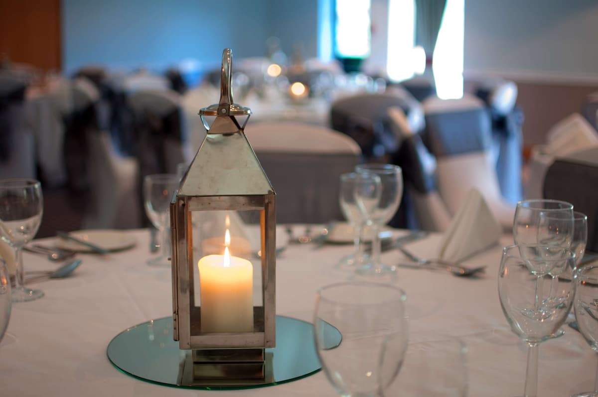Silver lantern centrepiece with lit candle on a dressed function room table.