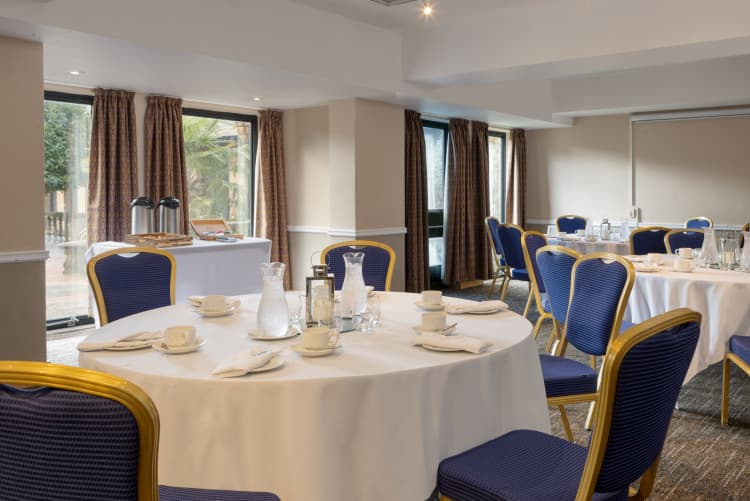 Round banquet tables with white linen and blue gold chairs in a function room.