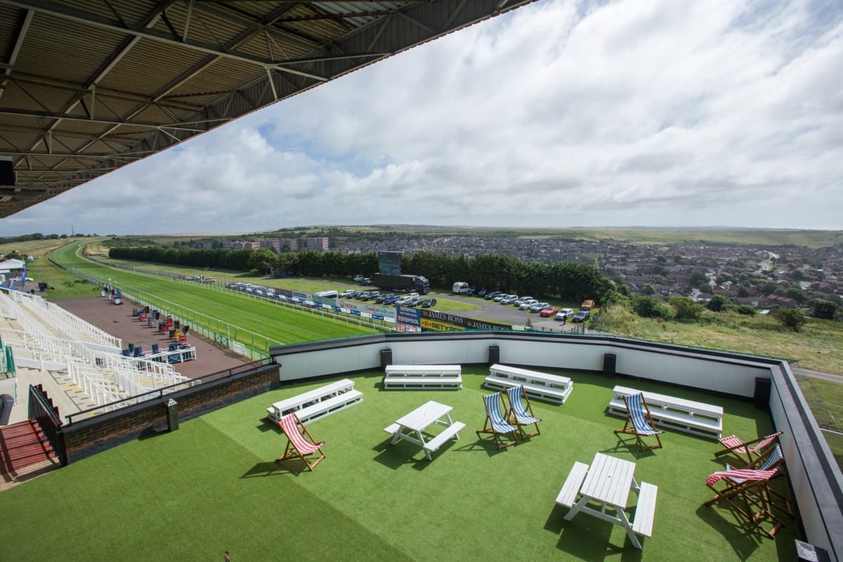 Rooftop terrace with deckchairs and picnic tables overlooking Brighton Racecourse track and town