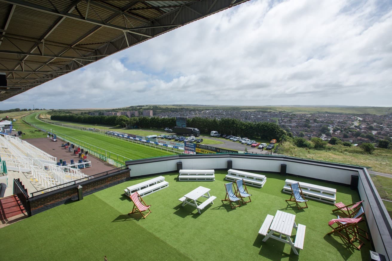 Rooftop terrace with deckchairs and picnic tables overlooking Brighton Racecourse track and town