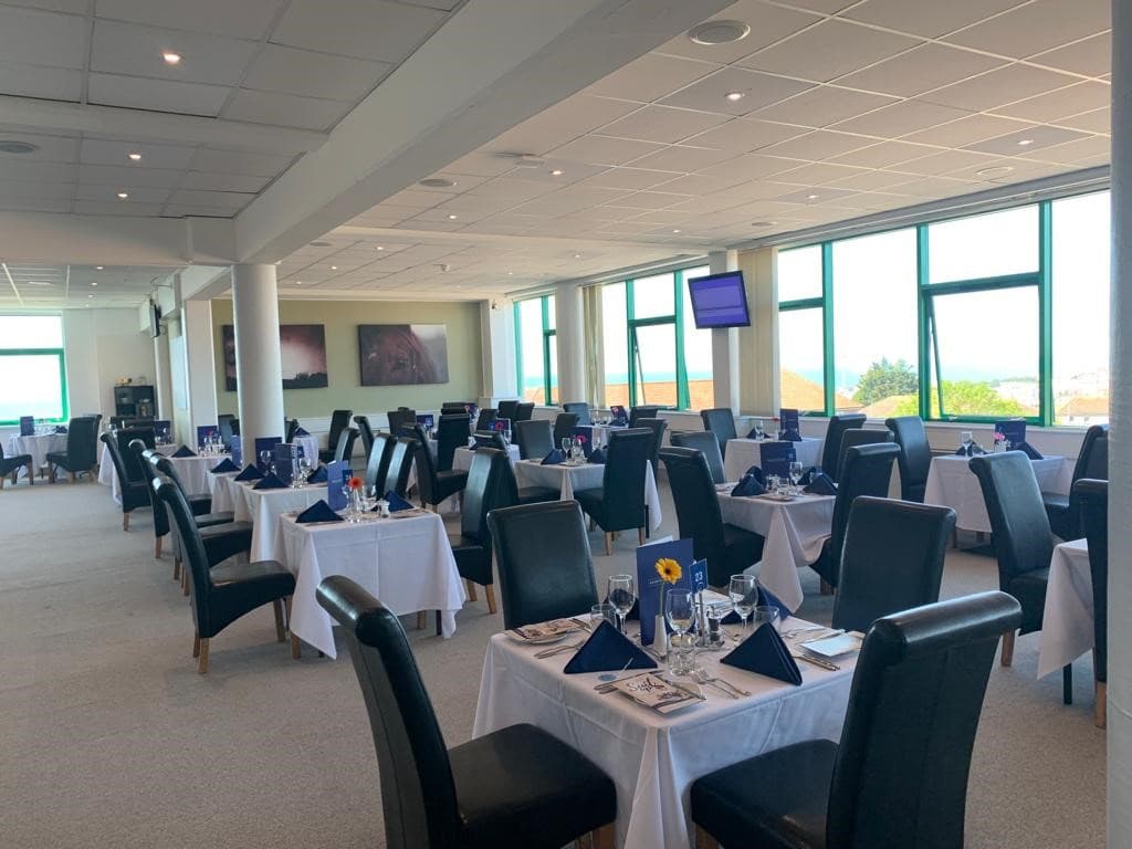 Bright function room at Brighton Racecourse with white-clothed tables set for dining.
