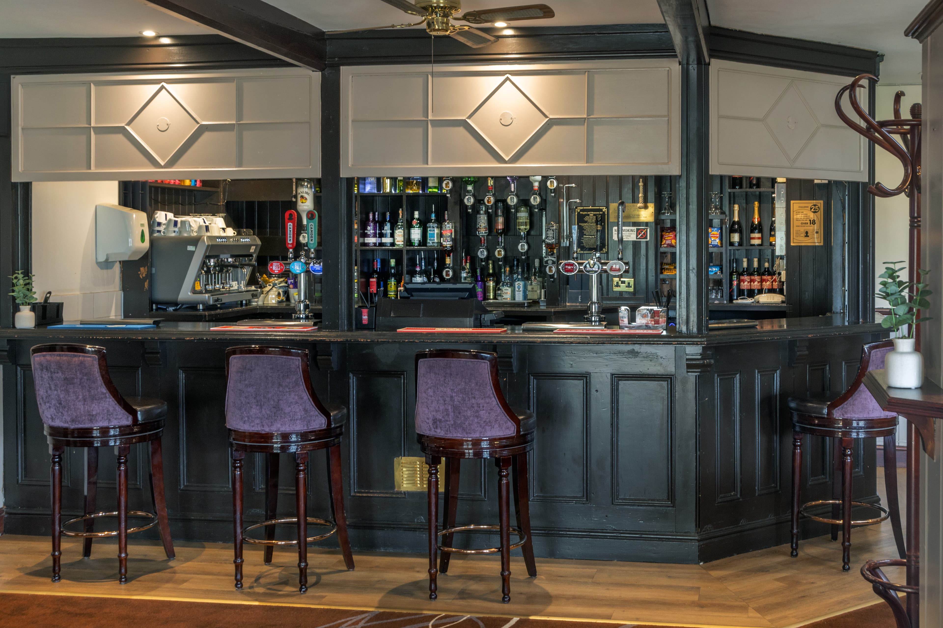 The bar at Calcot Hotel with dark wood panelling, bar stools and bottle shelves.