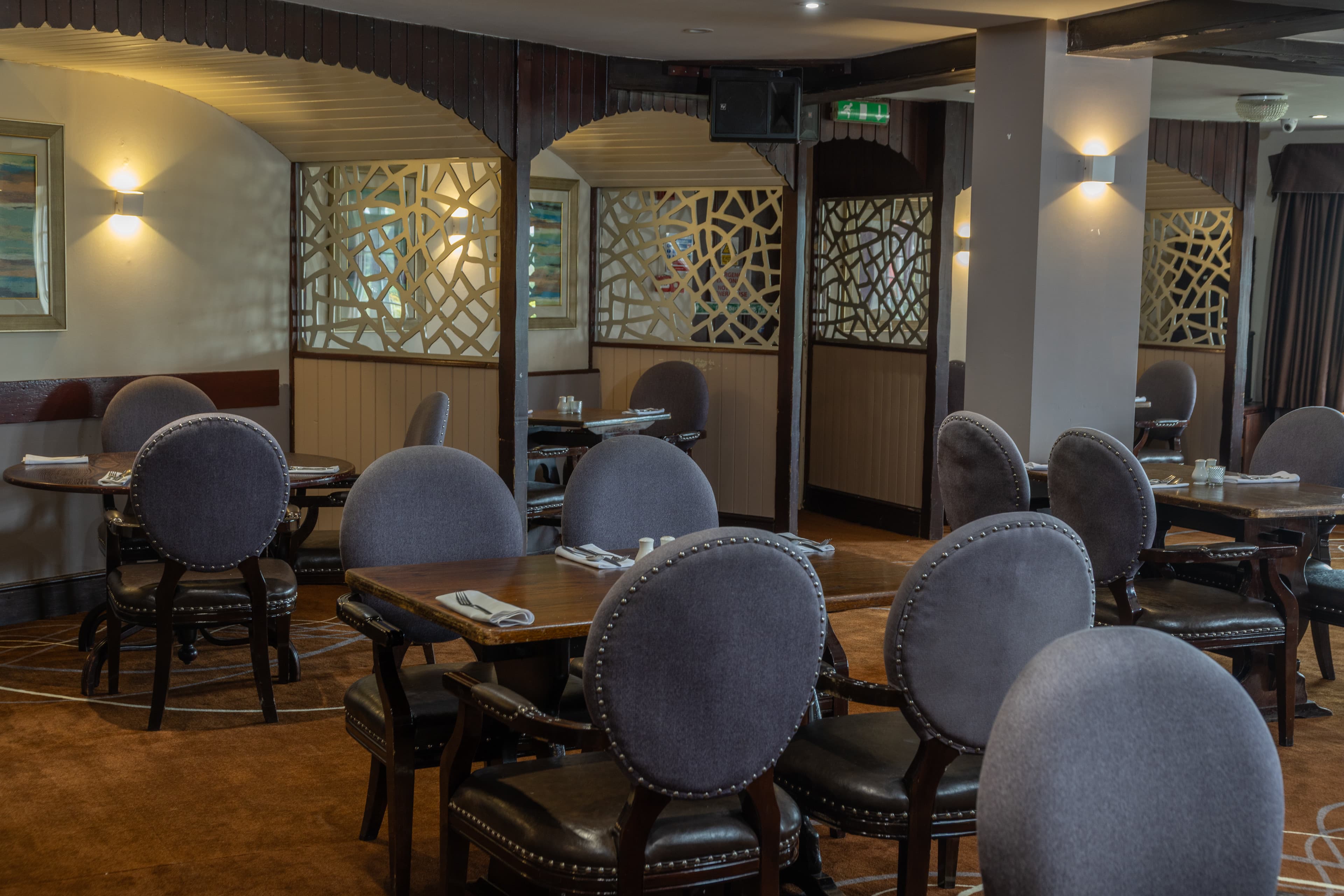 Dining room at Calcot Hotel with upholstered chairs, wooden tables and decorative screen partitions.