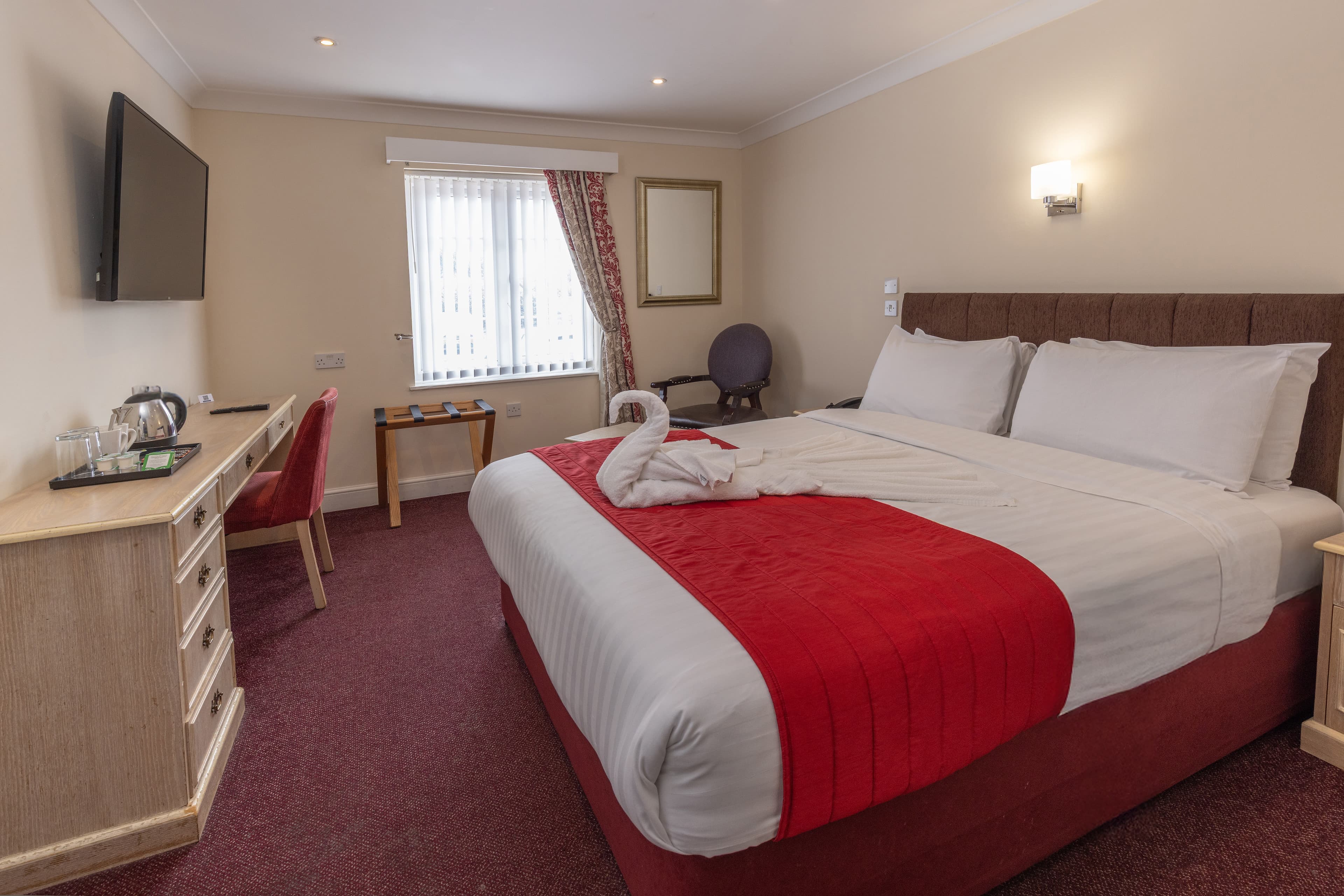 Double hotel room with red and white bed, wall-mounted TV and tea tray.