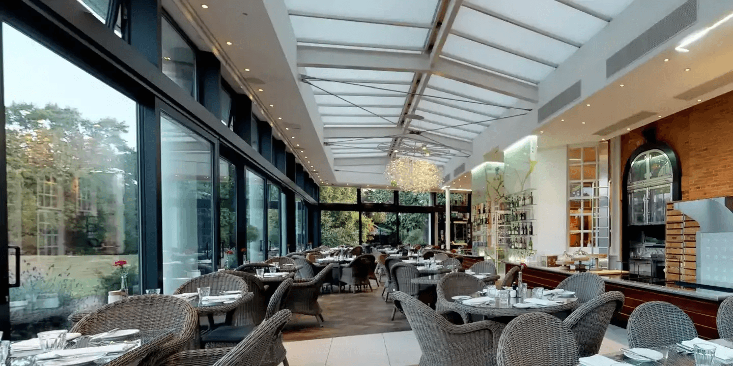 Glass-roofed restaurant dining room with wicker chairs overlooking a garden at Cannizaro House.