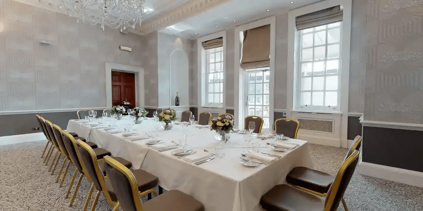 Private dining room with long white-clothed table, gold banquet chairs and floral centrepieces.