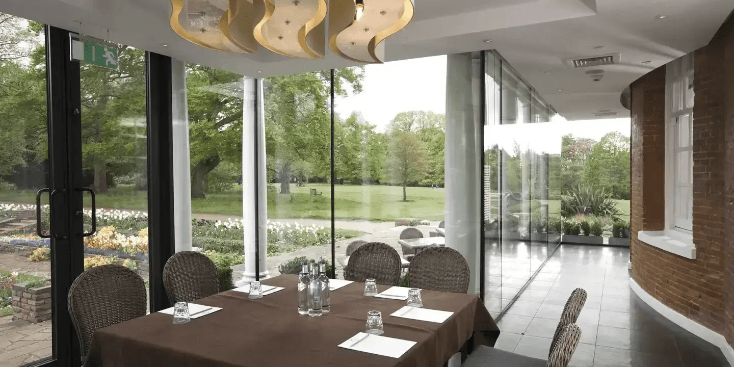 Glass-walled meeting room with garden views, set table and wicker chairs.