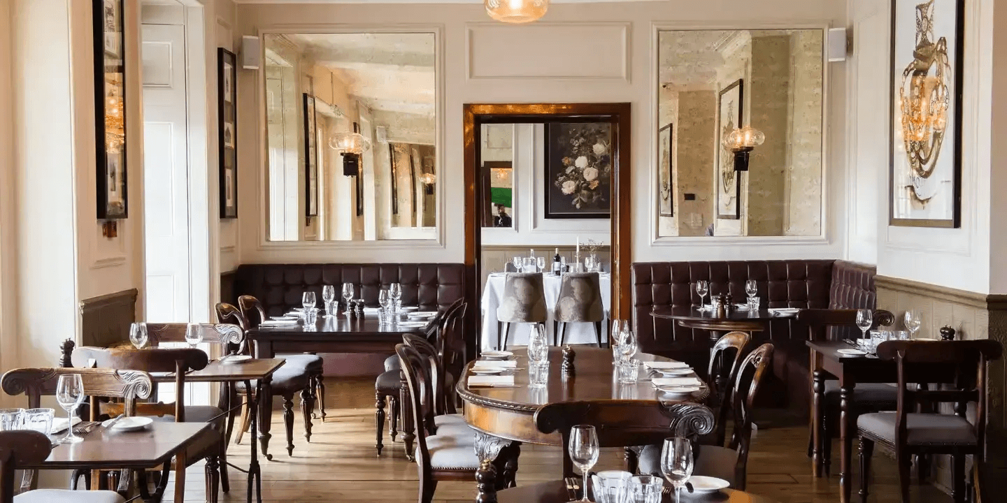 Elegant restaurant dining room with dark wood tables, banquette seating and antique mirrors.