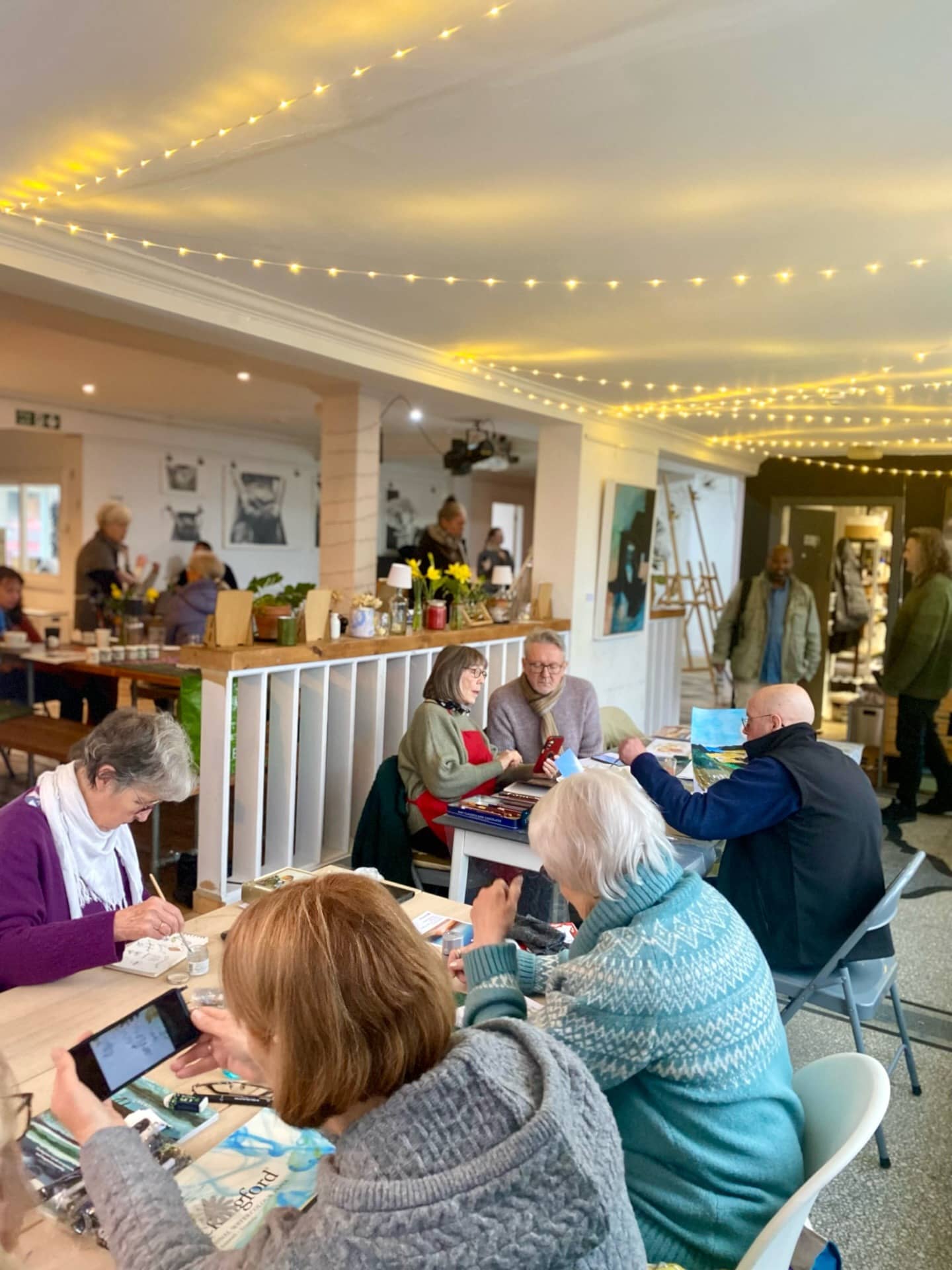 Adults taking part in an art workshop inside a warmly lit community hall.