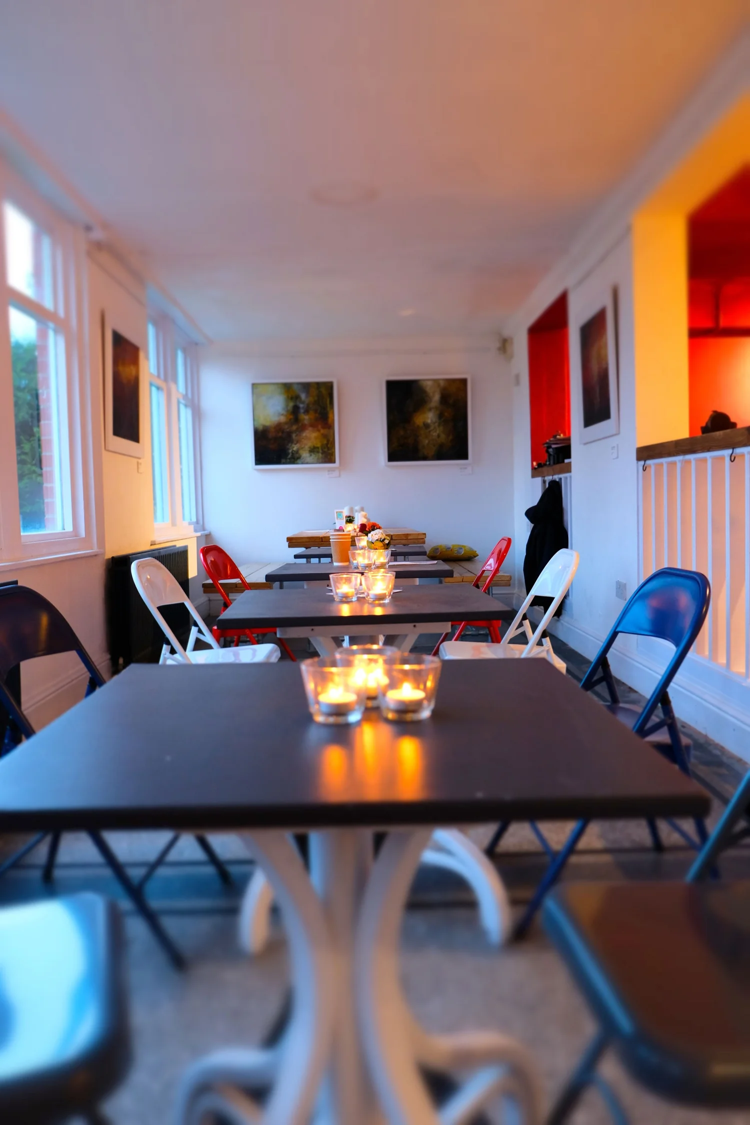 Candlelit dining room with dark tables, folding chairs and artwork on white walls.