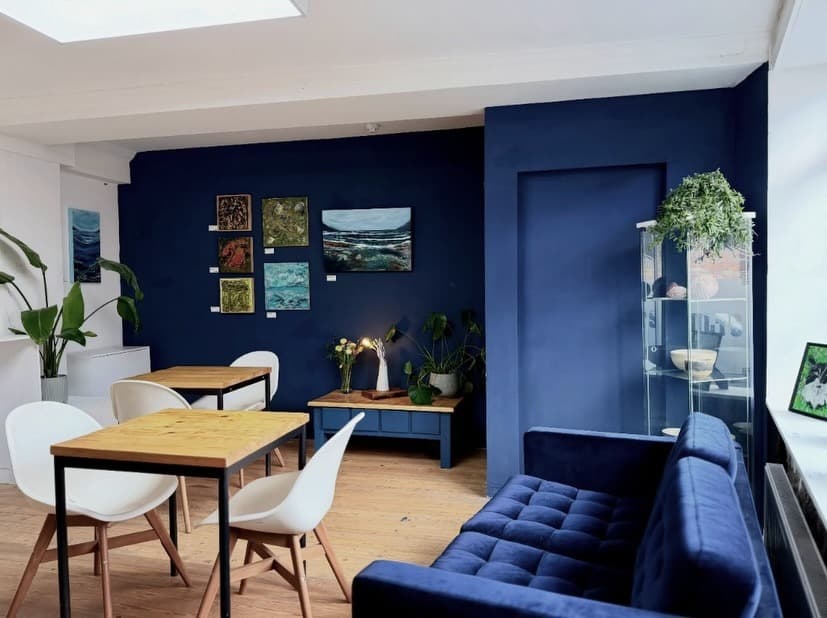 Bright interior with navy walls, wooden tables, white chairs and artwork displays.