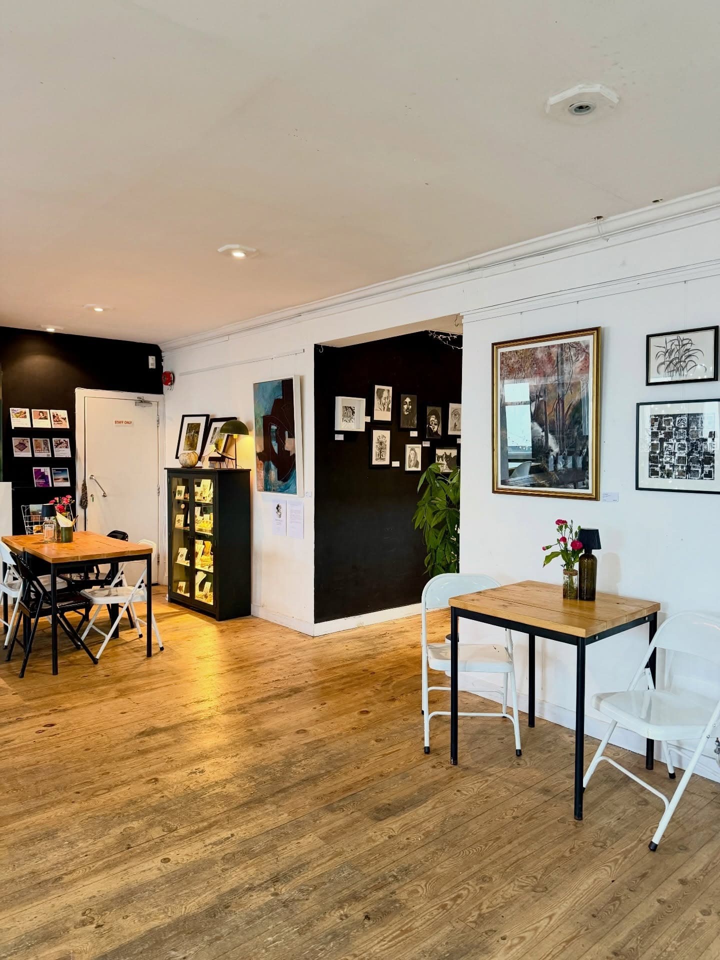 Light-filled gallery café space with wooden floors, small tables and artwork on walls.
