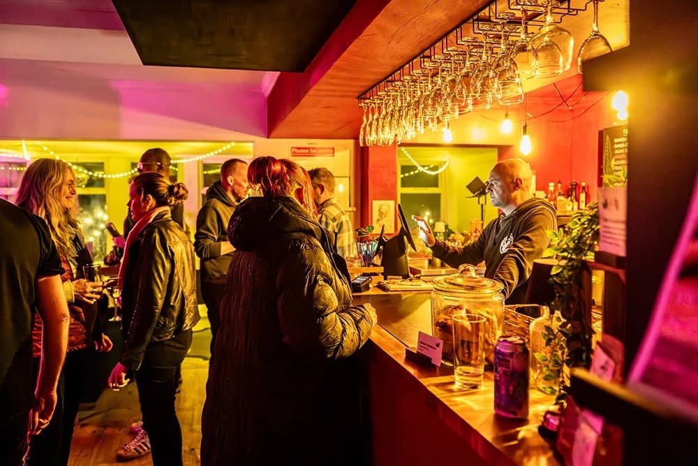 Guests gather at a warmly lit bar with wine glasses hanging overhead.