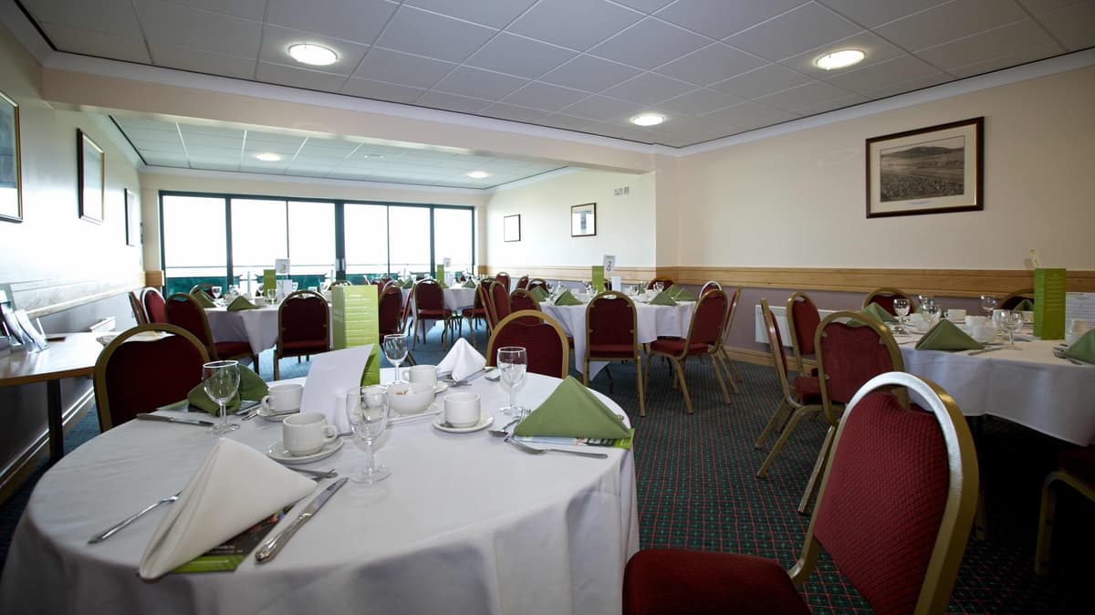Dining room at Chepstow Racecourse with round tables, white linen and red chairs.
