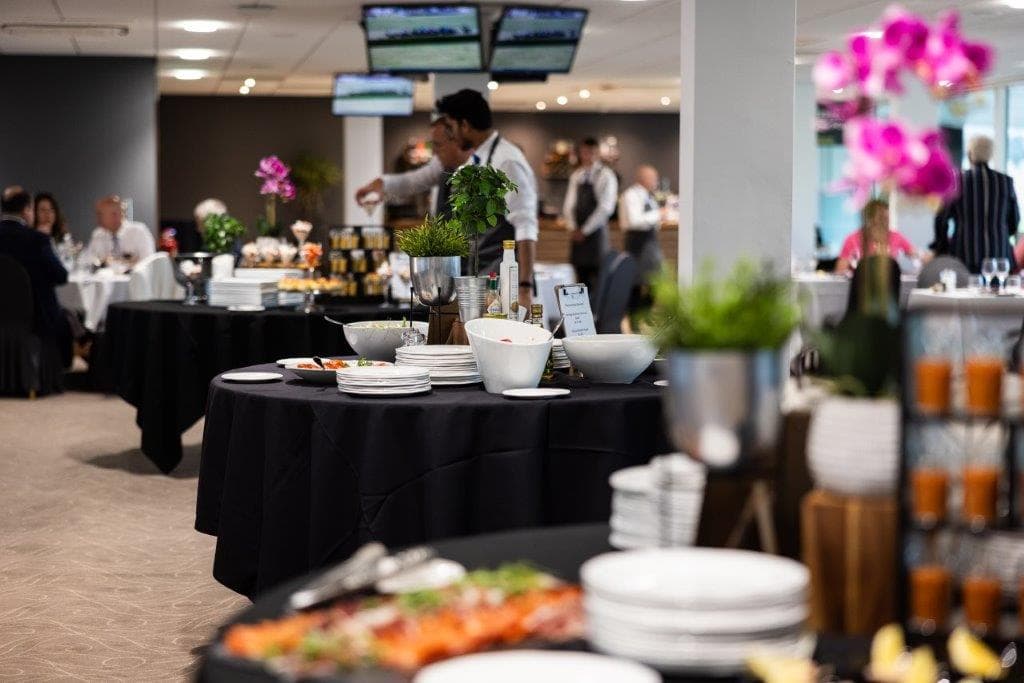 Buffet tables laid with white plates, salad bowls and pink orchid displays in a hospitality suite