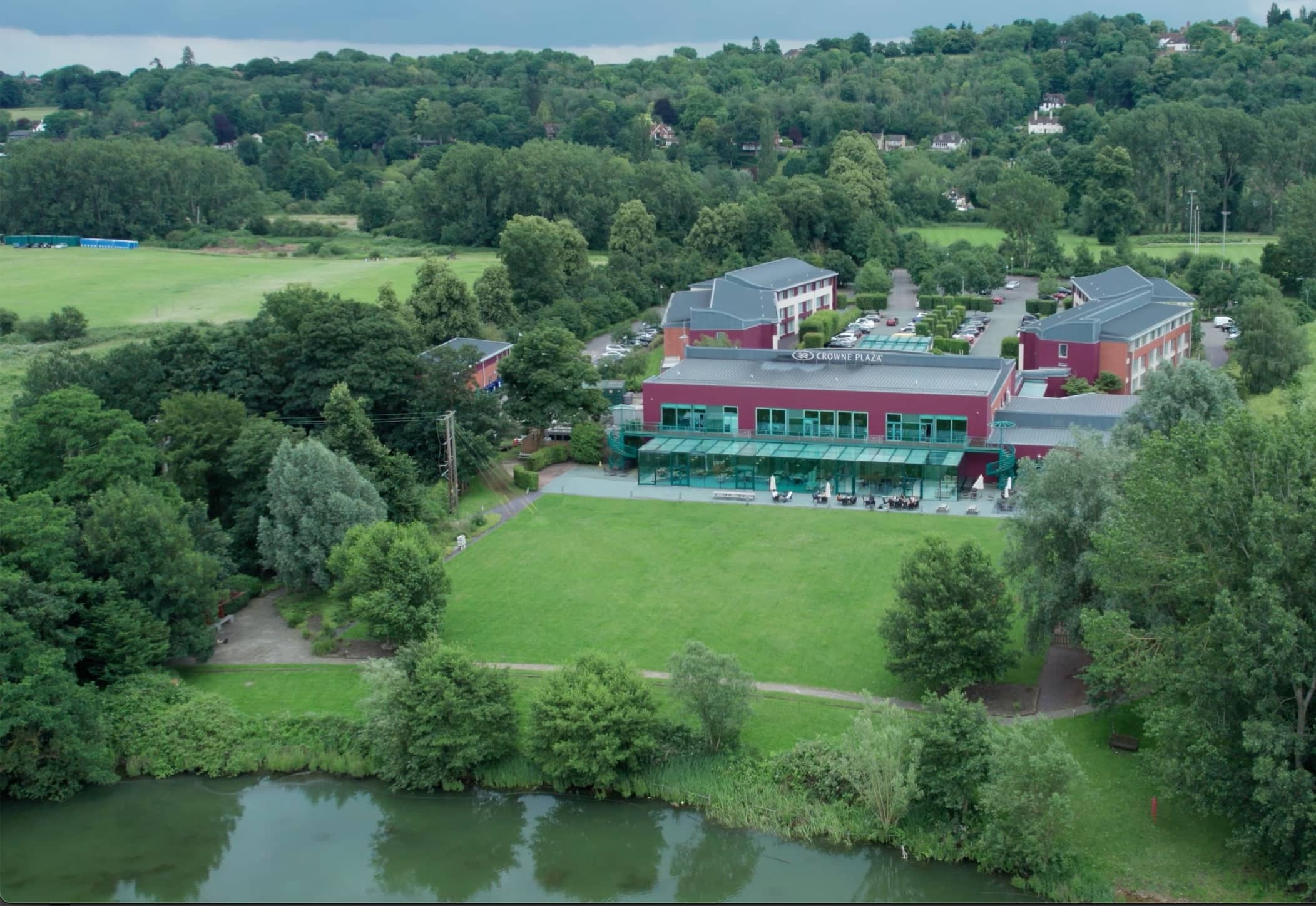 Aerial view of Crowne Plaza Marlow hotel beside a river with lawned grounds and trees.