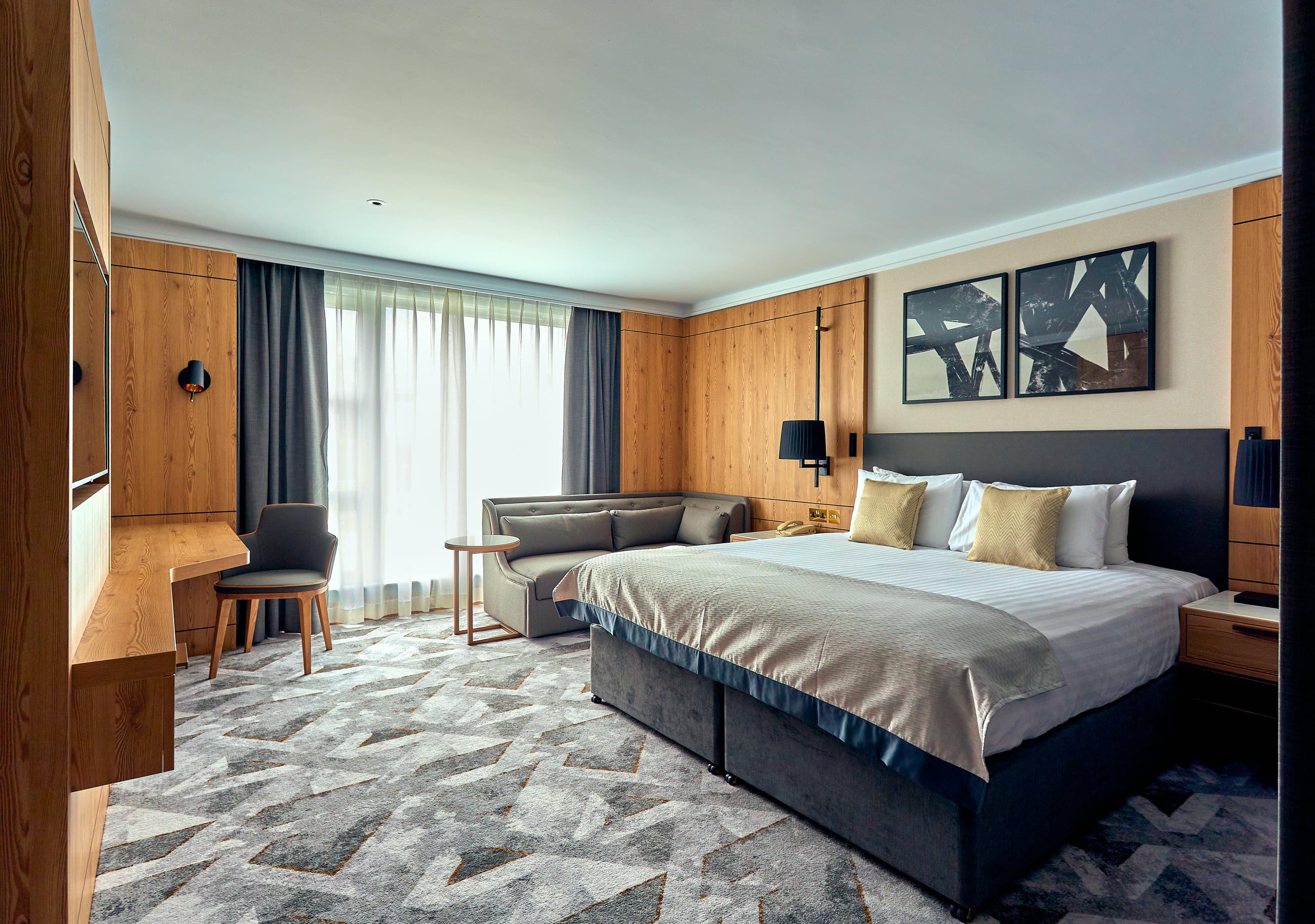 Spacious hotel bedroom with king-size bed, grey sofa and wood-panelled walls.