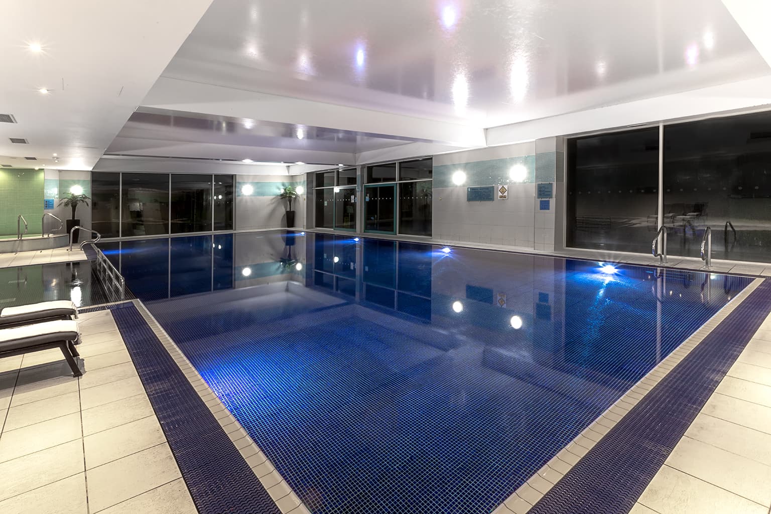 Indoor swimming pool with blue mosaic tiles and poolside loungers at Crowne Plaza Marlow.