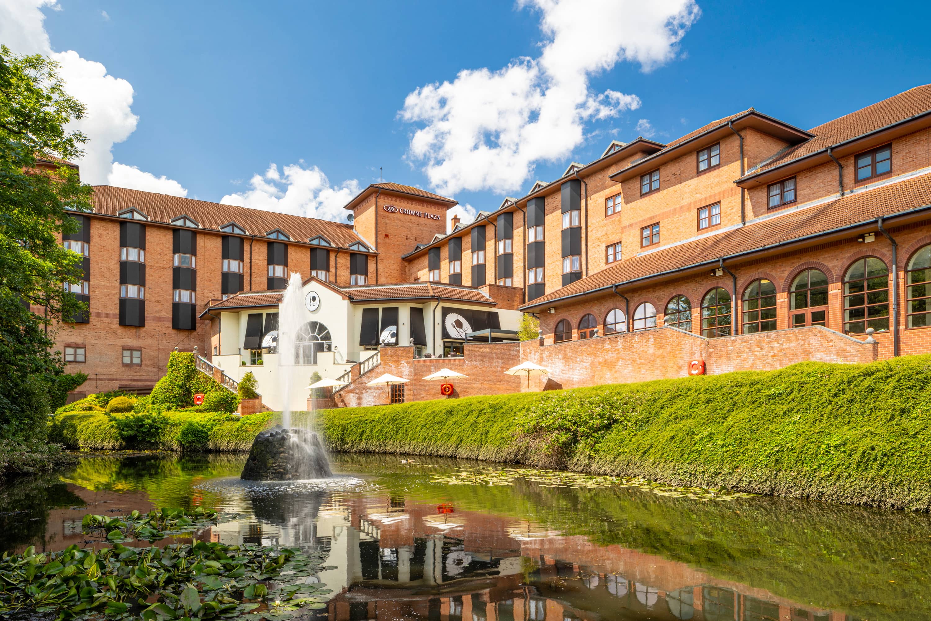 Crowne Plaza Solihull exterior with ornamental pond, fountain and lily pads in foreground.